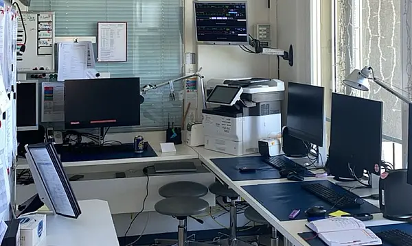 Ein moderner Büroraum mit mehreren Arbeitsplätzen, Computermonitoren und einem Drucker.